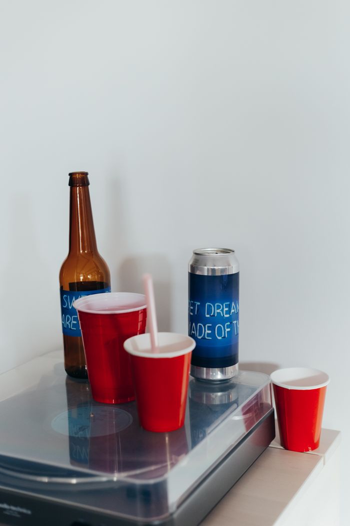 Arrangement of red cups, beer bottle, and can on a white table in a minimalist setting.