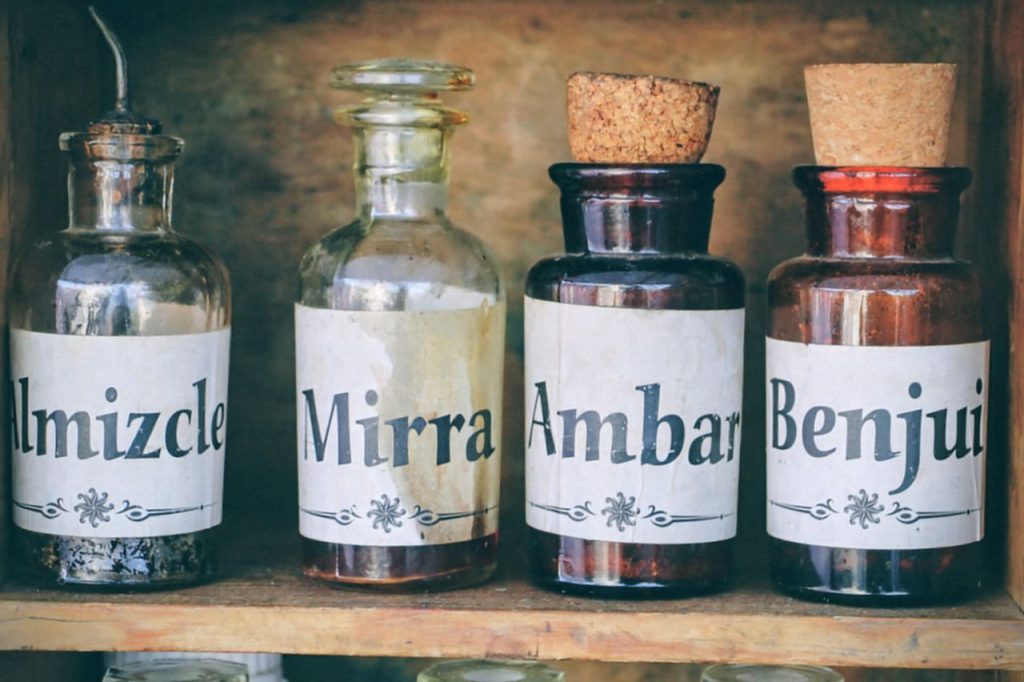 A collection of vintage apothecary bottles with labels 'Almizcle', 'Mirra', 'Ambar', and 'Benjui'.